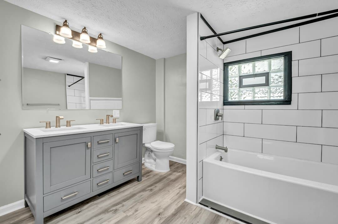 A bathroom with a grey double vanity, a white bathtub, and white subway tile walls — Photo by Josh Lemmon on Unsplash