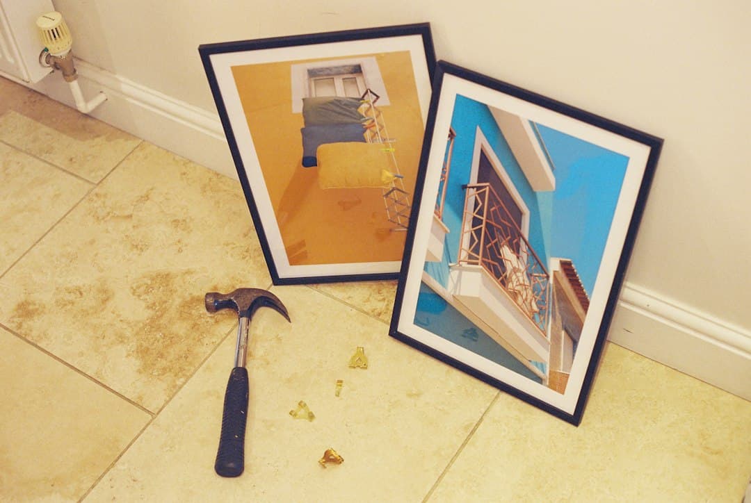 A hammer and brass picture hooks on a tiled floor near two framed prints — Photo by Barney Goodman on Unsplash