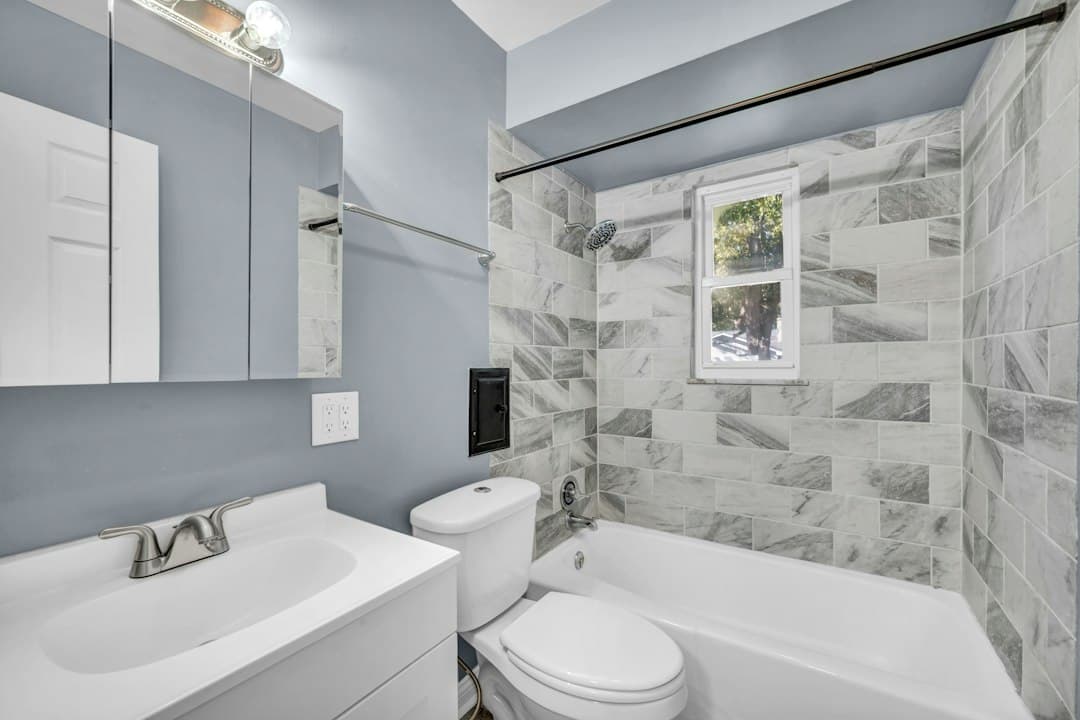 A bathroom with light blue walls, a white vanity, and a marble tiled shower area — Photo by Josh Lemmon on Unsplash